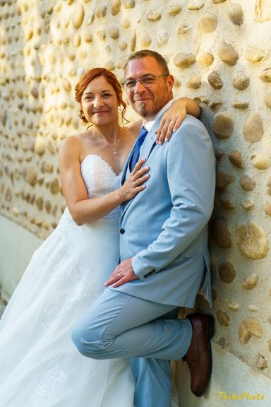 Un couple de mariés posant, le marié en costume clair et la mariée en robe blanche.